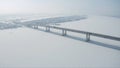 Aerial view of a long bridge above snow and ice covered river between two parts of a city. Clip. Winter landscape with a