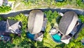 Aerial view of luxury hotel with straw roof villas and pools in tropical jungle and palm trees. Luxurious villa