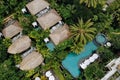 Aerial view of luxury hotel with straw roof villas and pools in tropical jungle and palm trees. Luxurious villa, pavilion in