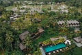 Aerial view of luxury hotel with straw roof villas and pools in tropical jungle and palm trees. Luxurious villa, pavilion in