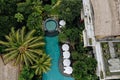 Aerial view of luxury hotel with straw roof villas and pools in tropical jungle and palm trees. Luxurious villa