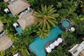 Aerial view of luxury hotel with straw roof villas and swimming pools in tropical jungle and palm trees. Luxurious villa