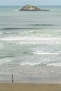 aerial view of man with surfboard going into ocean with lonely island in distance, Muriwai beach, Royalty Free Stock Photo