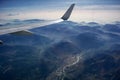 Aerial view of misty mountains, city, river, clouds and a plane wing, opposite the sunlight