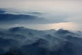 Aerial view of misty mountains, lake and clouds above the mountain peaks, opposite the sunlight, blue tinted