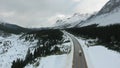 Aerial view of the motorhome moving along the road among snow-capped mountains and coniferous forest in Alberta, Canada