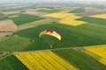 Aerial view motorized paraglider flying over canola fields in spring