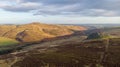 An aerial view of a mountain valley with grassy and stony slopes, trees and mountain range summits under a majestic blue sky and Royalty Free Stock Photo