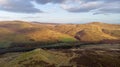 An aerial view of a mountain valley with grassy and stony slopes, trees and mountain range summits under a majestic blue sky and Royalty Free Stock Photo