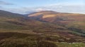 An aerial view of a mountain valley with grassy and stony slopes, trees and mountain range summits under a majestic blue sky and Royalty Free Stock Photo