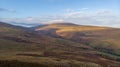 An aerial view of a mountain valley with grassy and stony slopes, trees and mountain range summits under a majestic blue sky and Royalty Free Stock Photo