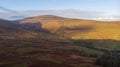 An aerial view of a mountain valley with grassy and stony slopes, trees and mountain range summits under a majestic blue sky and Royalty Free Stock Photo