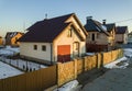 Aerial view of new residential house cottage and attached garage with shingle roof on fenced yard on sunny winter day in modern