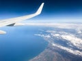 Aerial view of ocean through a plane window. Wing of airplane with blue sky and beauty clouds over the ocean. Aerial sea view Royalty Free Stock Photo