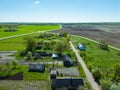 Aerial view over a small village near a dirt road. Large multi-colored fields planted with various agricultural crops. Wheat field