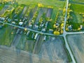 Aerial view over a small village near a dirt road. Large multi-colored fields planted with various agricultural crops. Wheat field