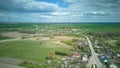 Aerial view over a small village near a dirt road. Large multi-colored fields planted with various agricultural crops. Wheat field