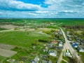 Aerial view over a small village near a dirt road. Large multi-colored fields planted with various agricultural crops. Wheat field