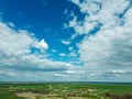 Aerial view over a small village near a dirt road. Large multi-colored fields planted with various agricultural crops. Wheat field