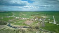 Aerial view over a small village near a dirt road. Large multi-colored fields planted with various agricultural crops. Wheat field