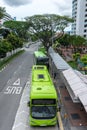 Aerial view from a overhead bridge of two green color public buses at bus stop allowing passengers to alight and board. These