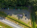 Aerial view of parking lot beside forest, with aligned vehicles, central triangular monument, hedges, and road markings blending Royalty Free Stock Photo