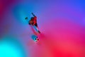 Aerial view of playing little boy during training with football ball in gradient red-blue neon light. Concept of action