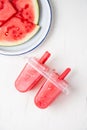 Aerial view of popsicle molds with ice cream, with plate with pieces of watermelon, vertical white background,