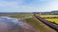 An aerial view of a railway track dam along a sandy beach and road under a majestic cloudy blue sky Royalty Free Stock Photo