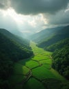 Aerial view of rich green valley with terraced fields. Sunbeams break through dramatic clouds, illuminating landscape. Scene Royalty Free Stock Photo