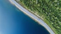Aerial view of road between green summer forest and blue lake. Blue car moving on road Royalty Free Stock Photo