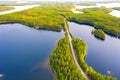 Aerial view of road between green summer forest and blue lake in Finland