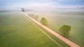 Aerial view of rural dirt road and trees covered by fog. Early misty morning. Spring summer fields. Rainy overcast moody weather Royalty Free Stock Photo