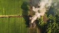 An aerial view of a rural landscape with a small mobile factory parked in a field of vibrant green crops. Smoke billows Royalty Free Stock Photo