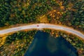 Aerial view of rural road with red car in yellow and orange autumn forest with blue lake Royalty Free Stock Photo