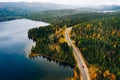 Aerial view of rural road with red car in yellow and orange autumn forest with blue lake Royalty Free Stock Photo