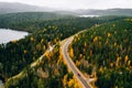 Aerial view of rural road with red car in yellow and orange autumn forest with blue lake Royalty Free Stock Photo