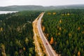 Aerial view of rural road with red car in yellow and orange autumn forest with blue lake Royalty Free Stock Photo