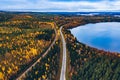 Aerial view of rural road with red car in yellow and orange autumn forest with blue lake Royalty Free Stock Photo