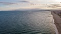 An aerial view of a sandy beach and blue water sea with an urban sea coast area in the background at sunset with ray of light Royalty Free Stock Photo