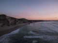 Aerial view of sea waves breaking sandy beach surrounded by hills during sunset Royalty Free Stock Photo