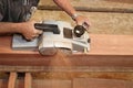 Aerial view of senior carpenter using electric planer with wooden plank in carpentry workshop. Selective focus and shallow depth o