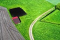 Aerial view of a shed behind a small artificial fish pond on a path through a green meadow next to a field, abstract effect