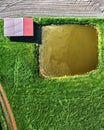 Aerial view of a shed behind a small artificial fish pond on a path through a green meadow next to a field, abstract effect