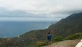 Aerial view. A single man stands on the edge of a mountain, looking at a beautiful view - the long coast of the Atlantic