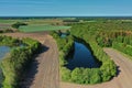 Aerial view of a small dark blue pond with high trees on the bank between fields and the flat North German landscape on the