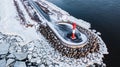 Aerial view of a small red lighthouse in the sea surrounded by breakwaters and ice