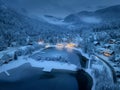 Aerial view of snowy village, trees, lake, street lights at night Royalty Free Stock Photo