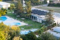 aerial view of solar array on the rooftop of a tourist resort building with lodging and swimming pools. blue water, empty pools