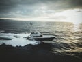 Aerial view of a sportfishing boat sailing in a blue tranquil sea under a cloudy sky at sunset